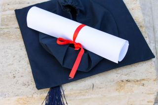 Diplôme roulé noué de rouge posé sur une toque