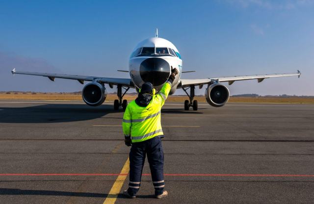 Devenir agent de piste ou agent d'escale sur un aéroport Placeur en gilet jaune qui guide un avion avec ses bâtons
