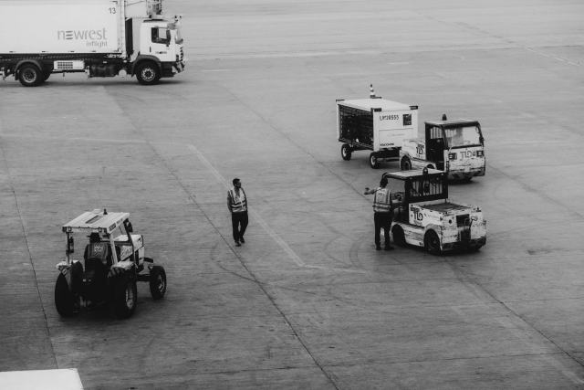 Trouver un emploi d'aéroport sans diplôme : métiers et étapes Agents et tracteurs à bagages sur l'aire de trafic, en noir et blanc
