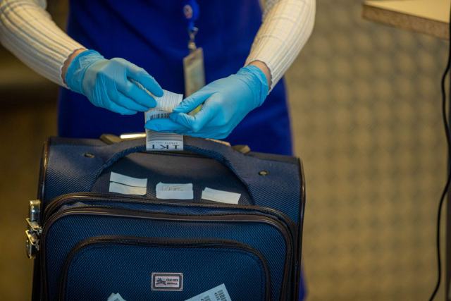 Devenir agent de sûreté aéroportuaire : le parcours complet Agent en gants bleus qui inspecte un bagage cabine